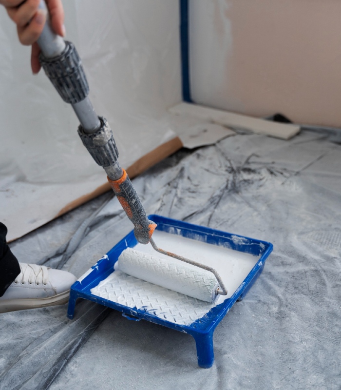 Artisan peintre en bâtiment utilisant un rouleau pour appliquer une peinture blanche sur chantier – Artisan Pachet